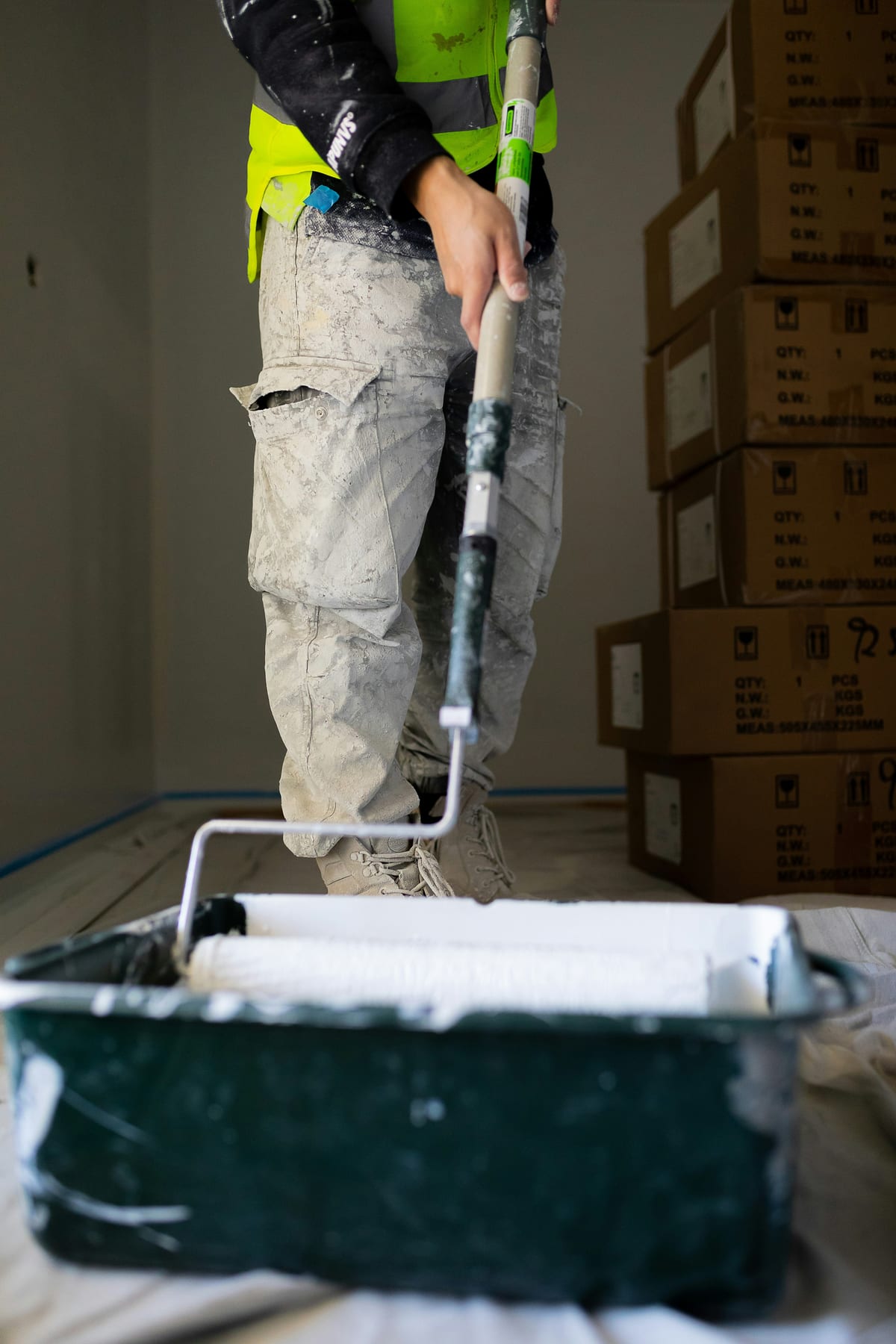 Professional painter in work clothes holding an extension pole paint roller dipped in white ceiling paint with a roller tray