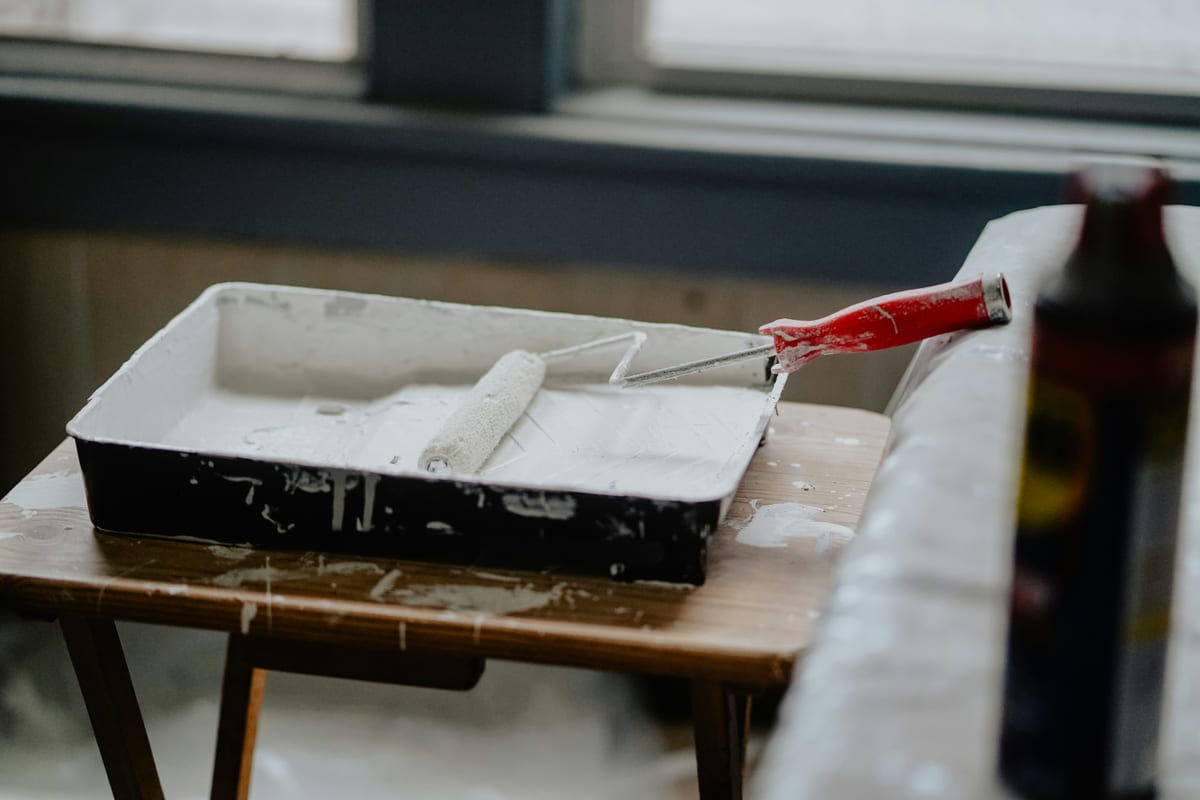 Paint roller frame sitting in a roller tray filled with white ceiling paint on a work stand